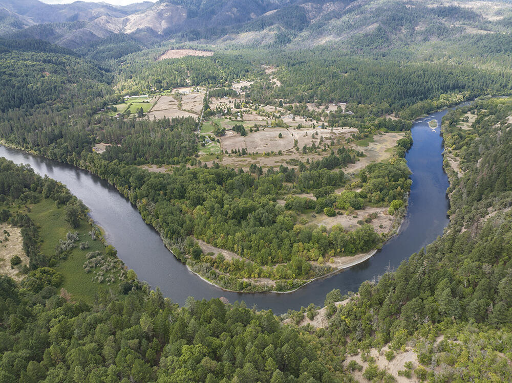 Aerial view of wooded land along a broad river bend, open fields, and distant mountains.