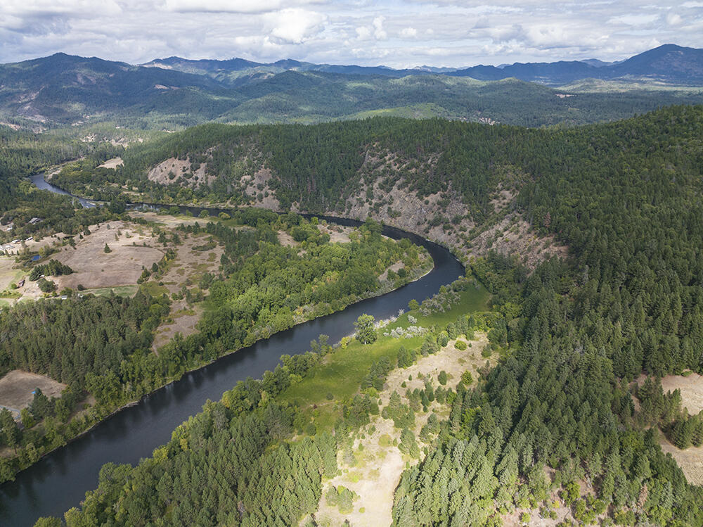 Aerial view of a winding river through forested hills and open clearings.