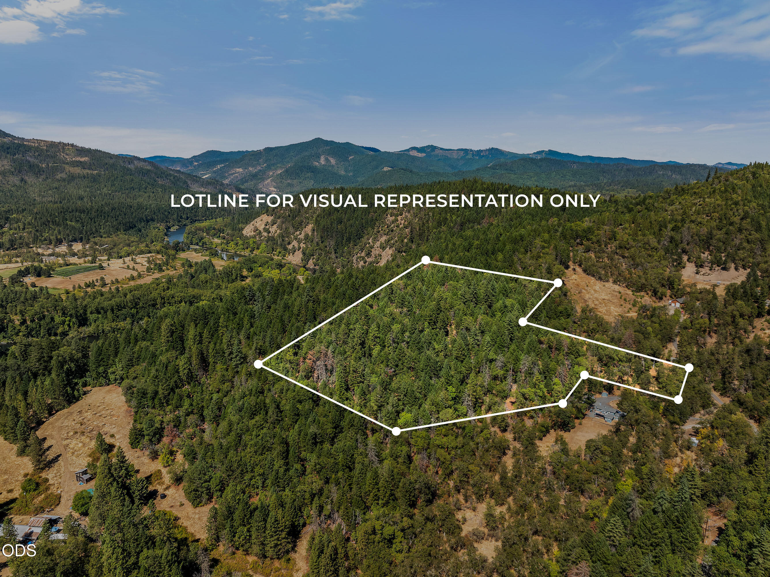 Aerial view of wooded land outlined in white, with forested hills and mountains beyond.