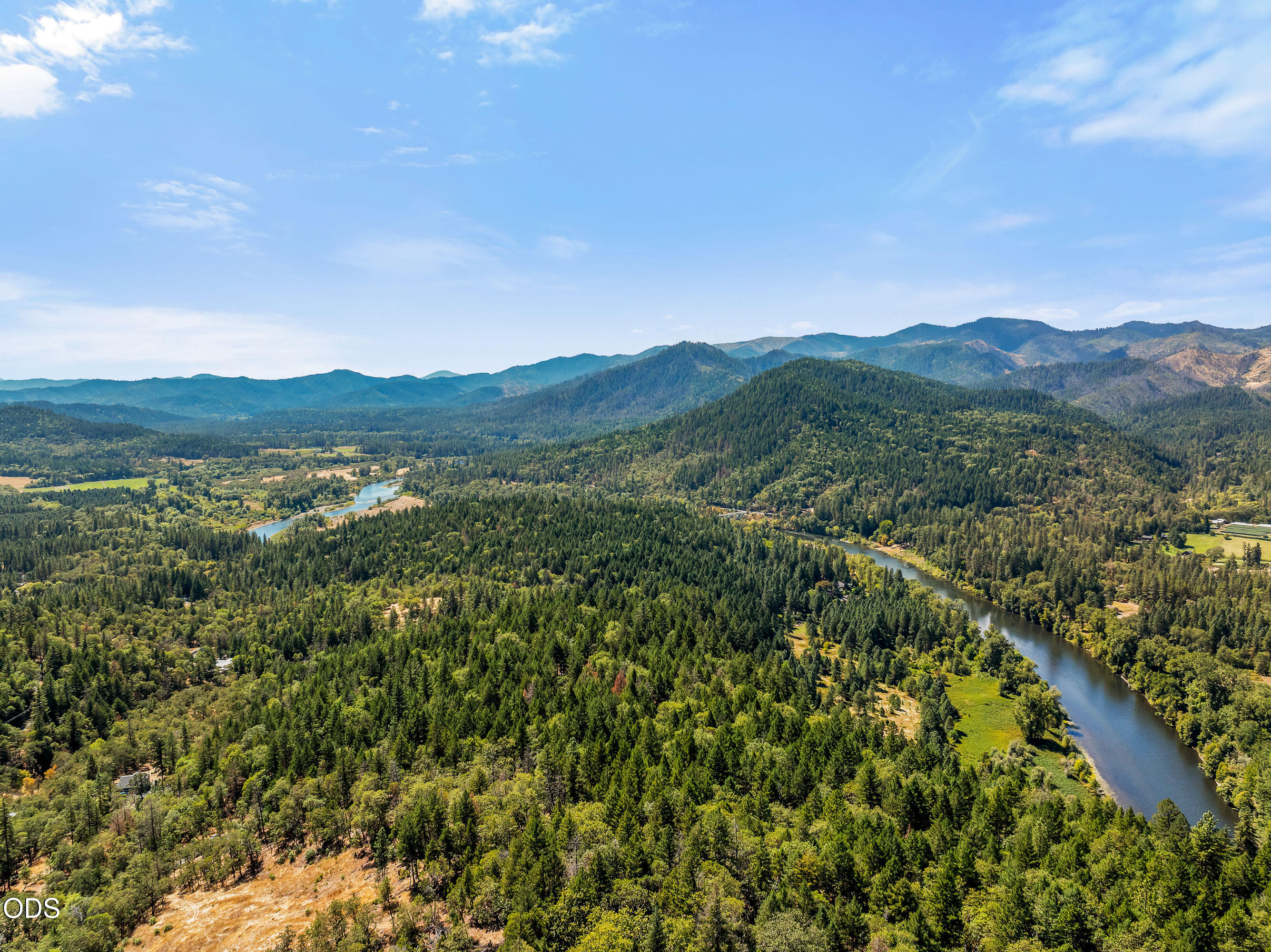 Aerial view of a forested valley with a winding river and distant mountains.