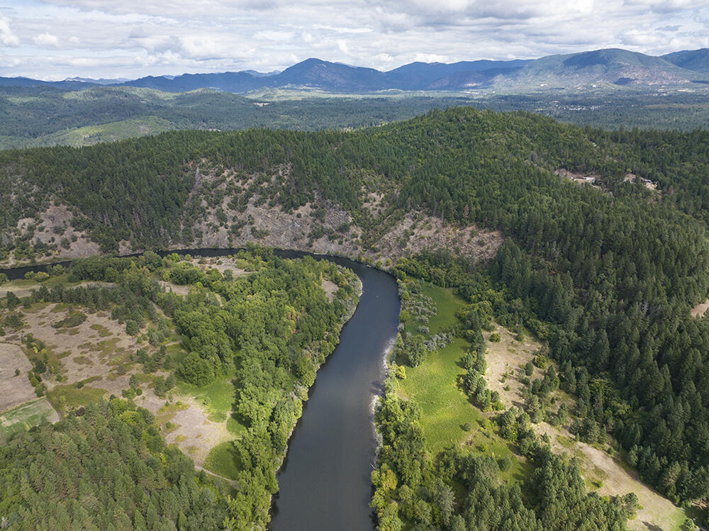 A river curves through forest and open fields, with mountain ranges in the distance.