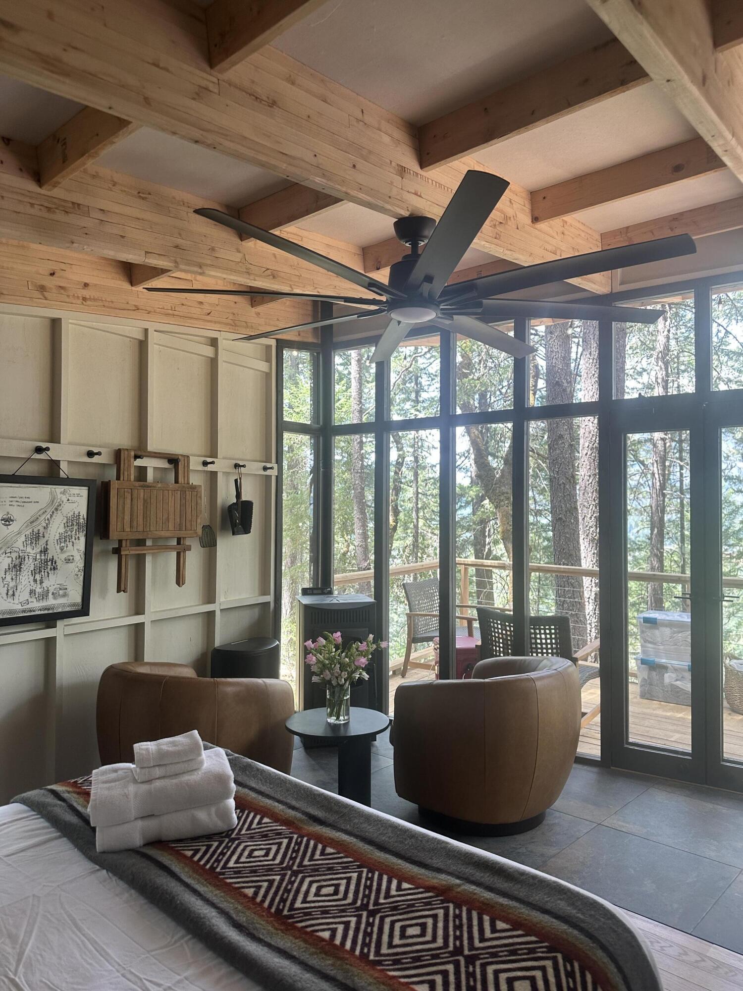 Bedroom with exposed timber beams, floor-to-ceiling windows, and a wooded view from the deck.