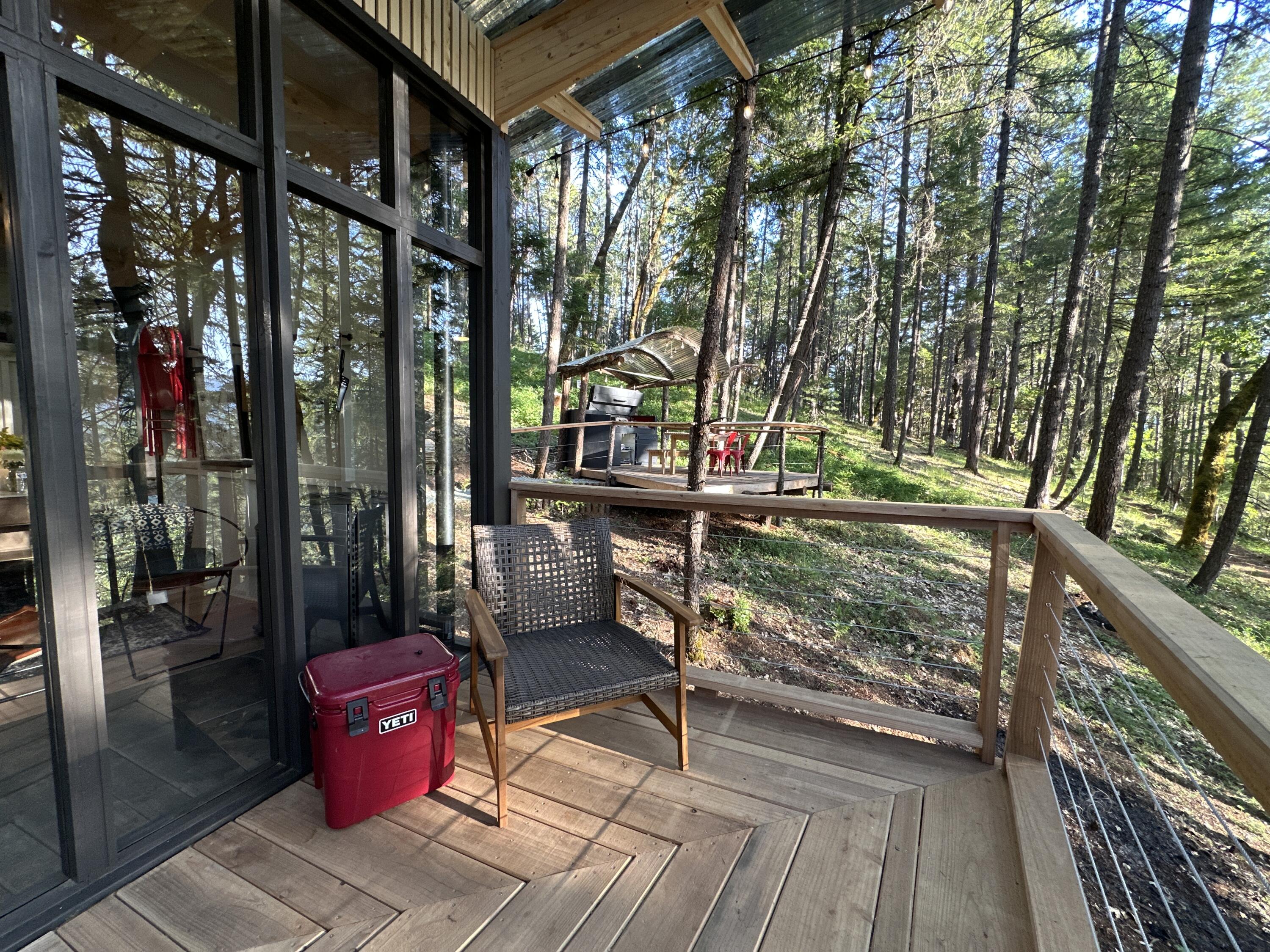 Wooden deck with a woven chair and red cooler overlooking a wooded hillside.