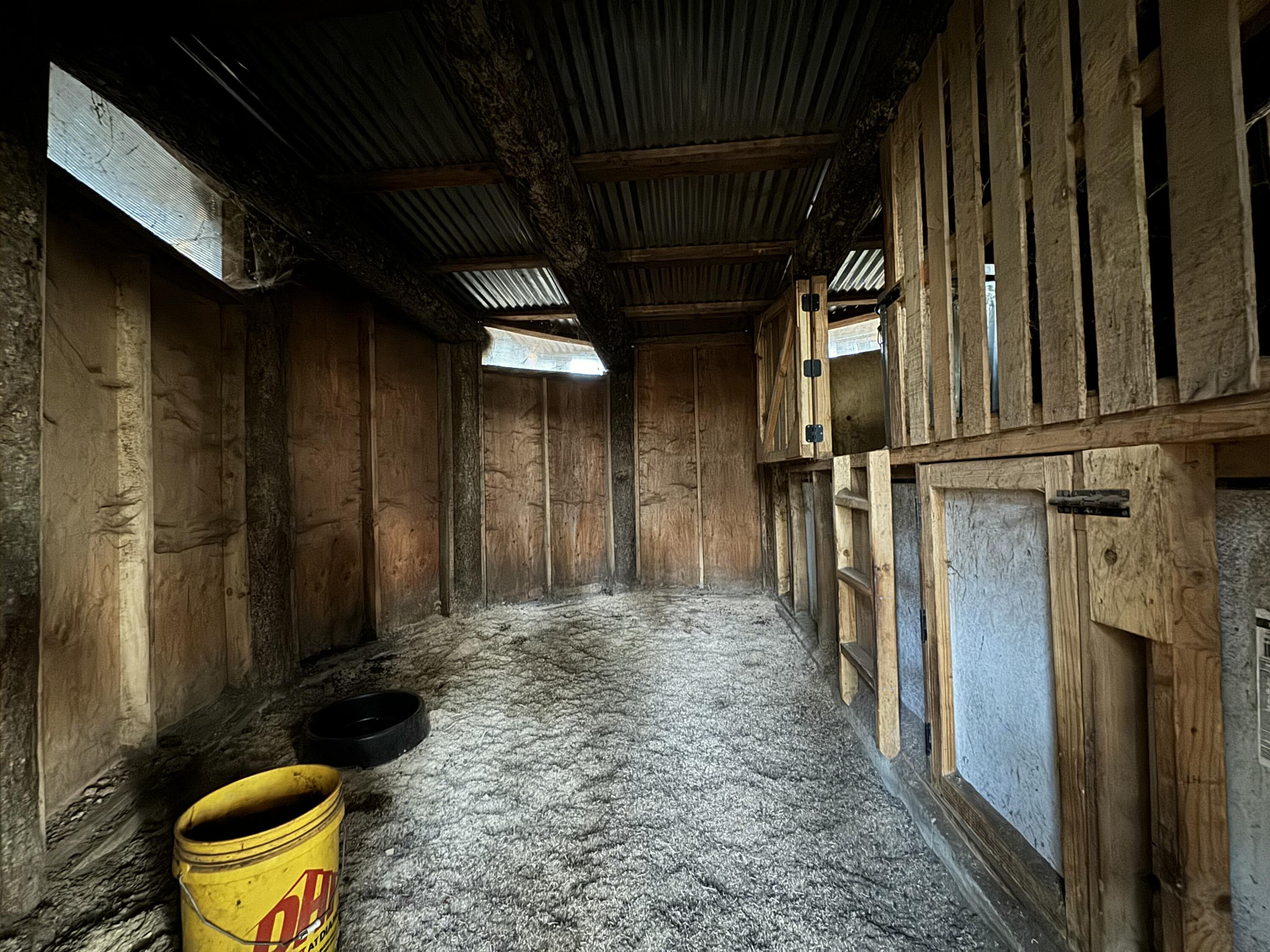 Rustic wooden barn interior with a gravel floor, stall partition, and buckets.