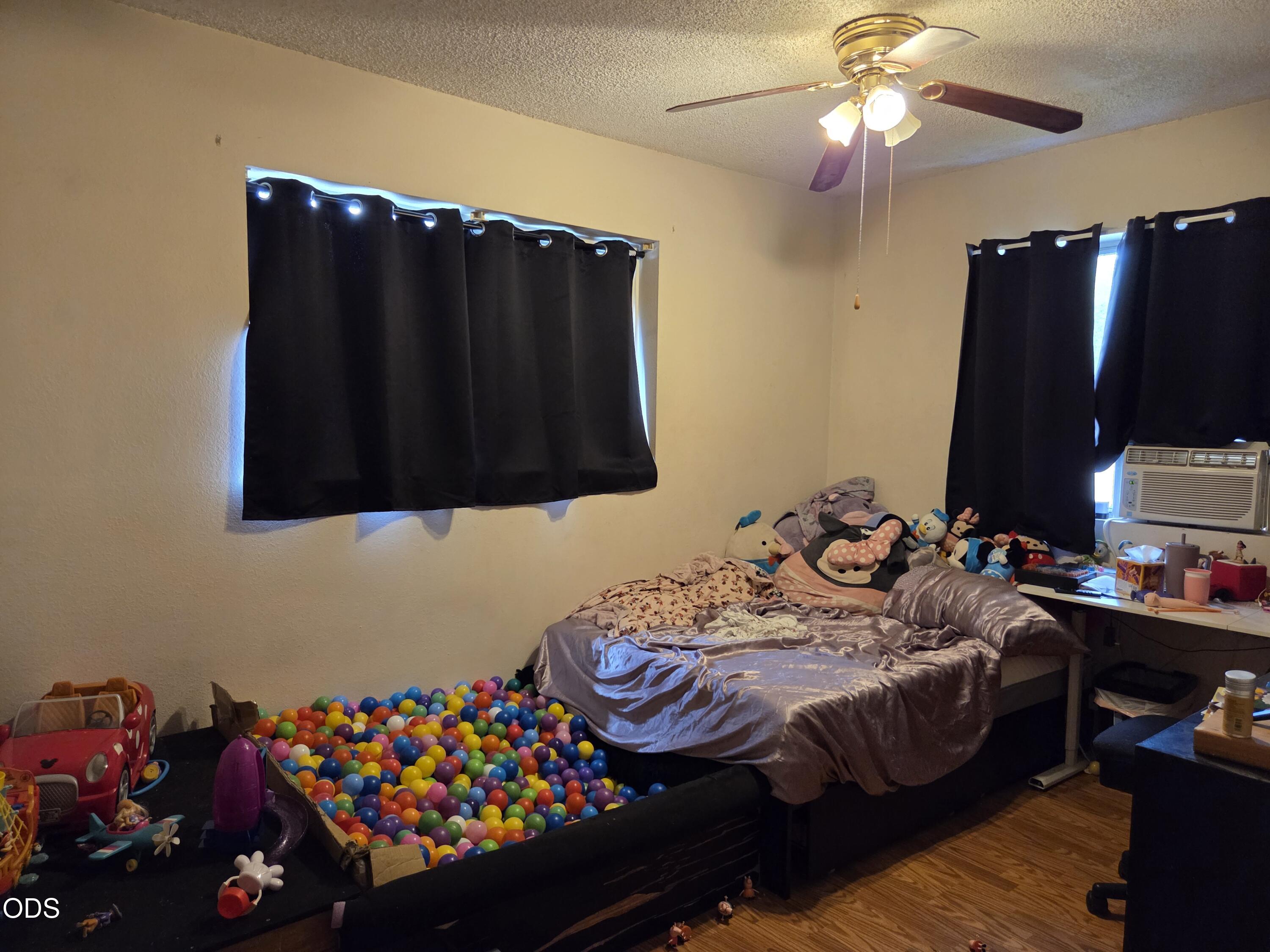 Bedroom with a colorful ball pit beside a bed and toys scattered around the room.