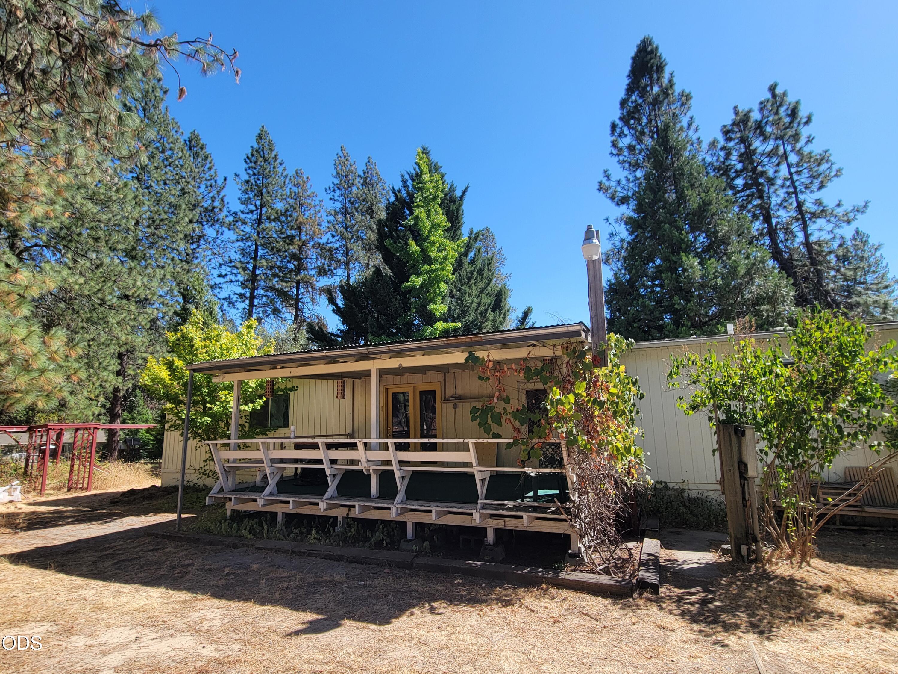 Grants Pass home with a long covered porch, wooden railing, and tall pine trees.