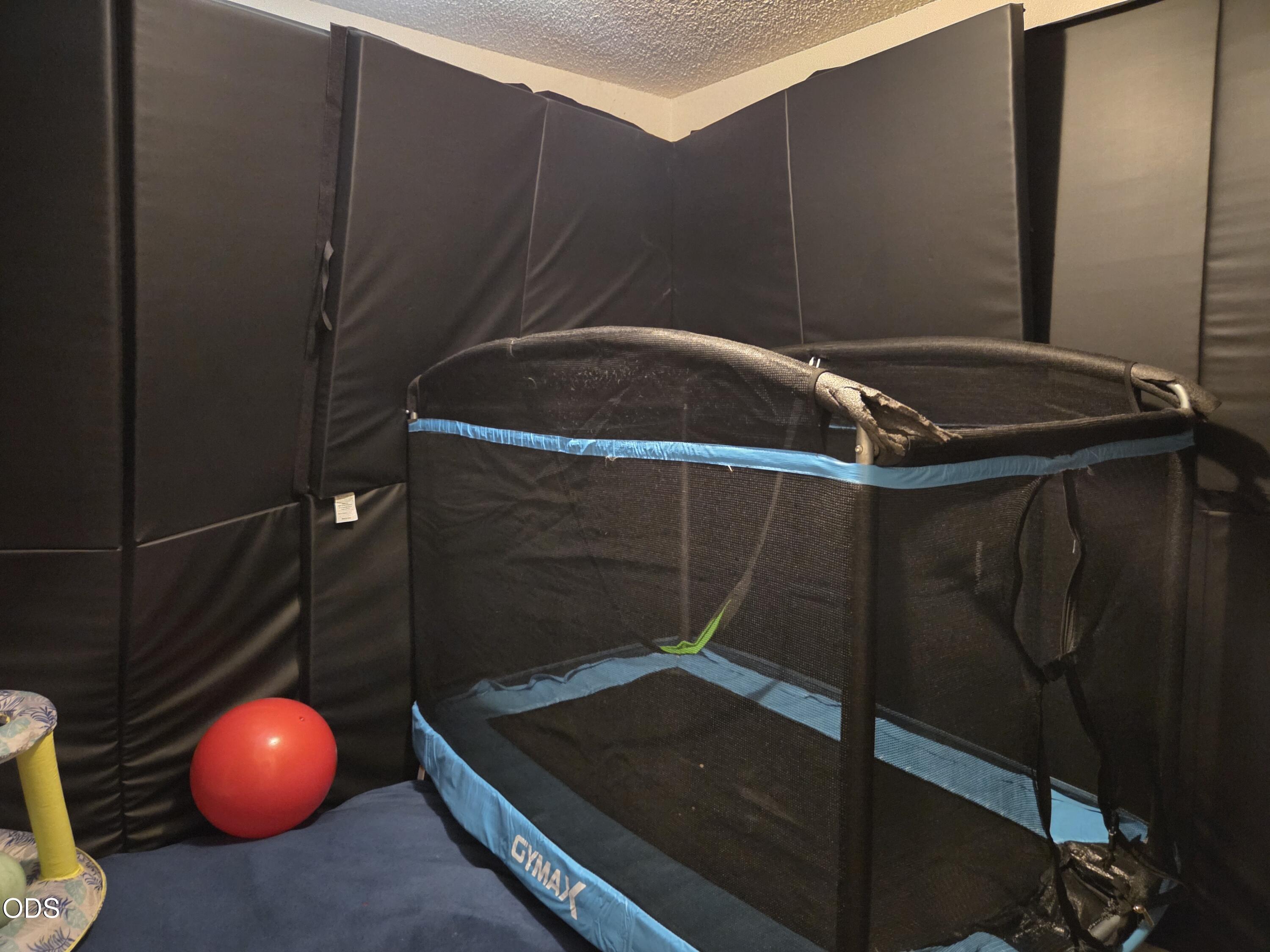Indoor play area with a large enclosed trampoline, padded walls, and a red exercise ball.