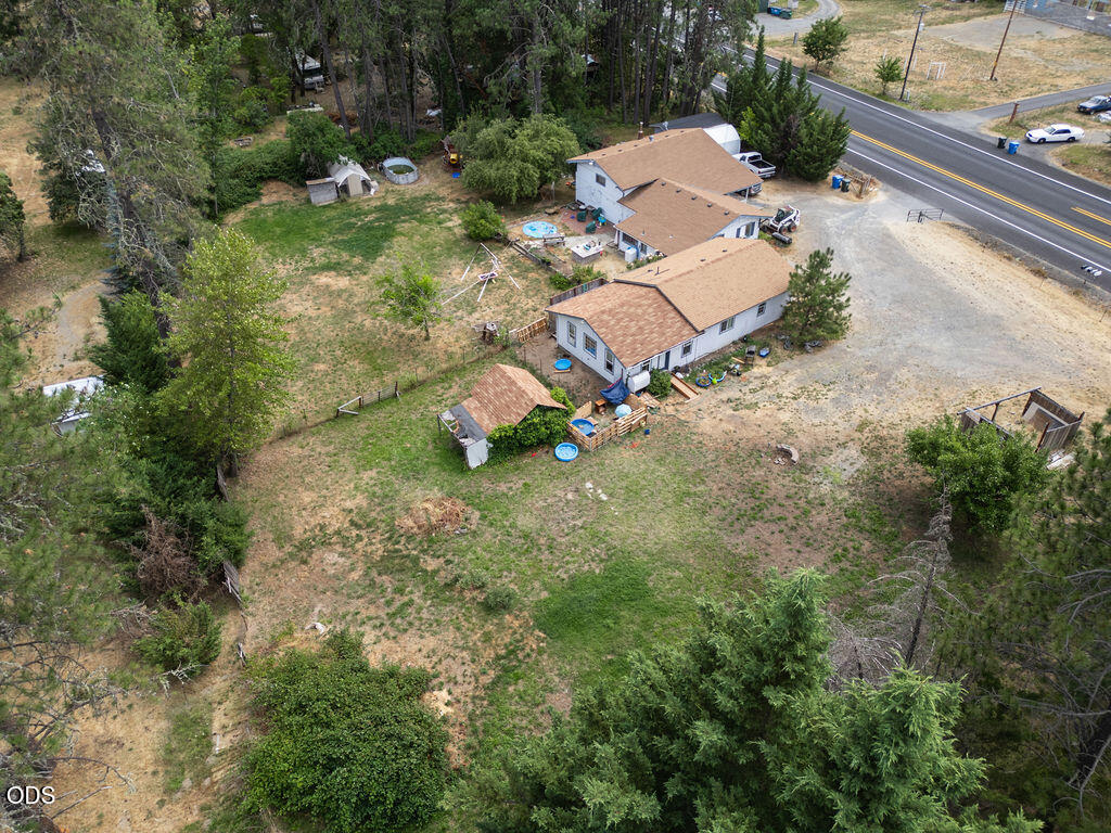 Aerial view of two houses on a large tree-bordered lot beside a road.