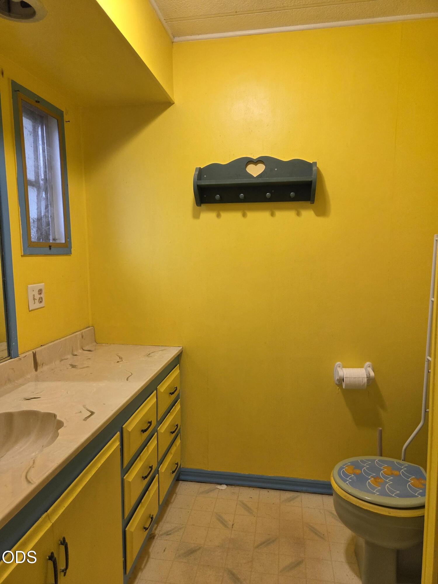 Bathroom with vivid yellow walls, blue-trimmed vanity, and a toilet with a patterned seat.