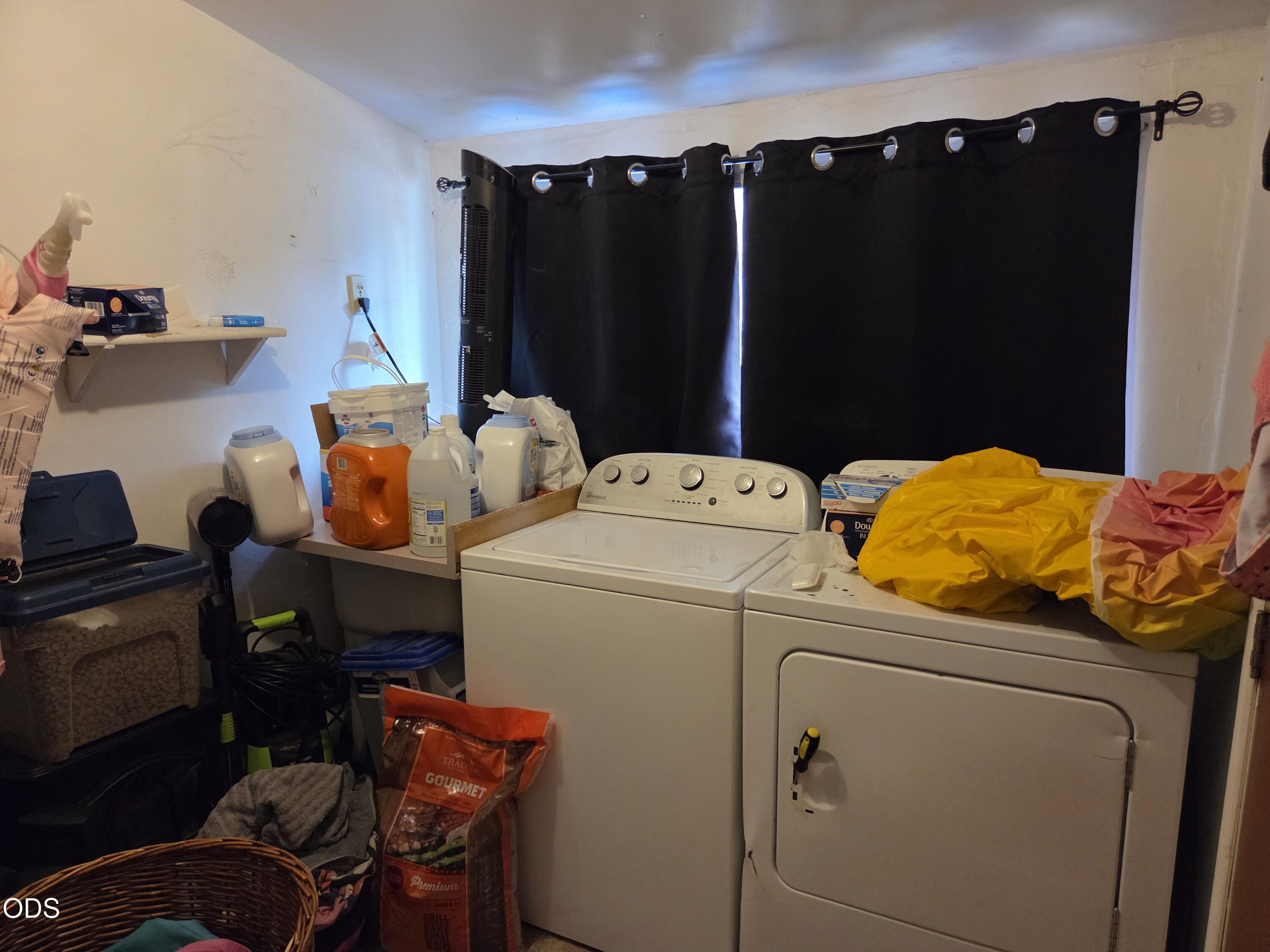 Laundry room with a top-loading washer, front-loading dryer, and black curtains.