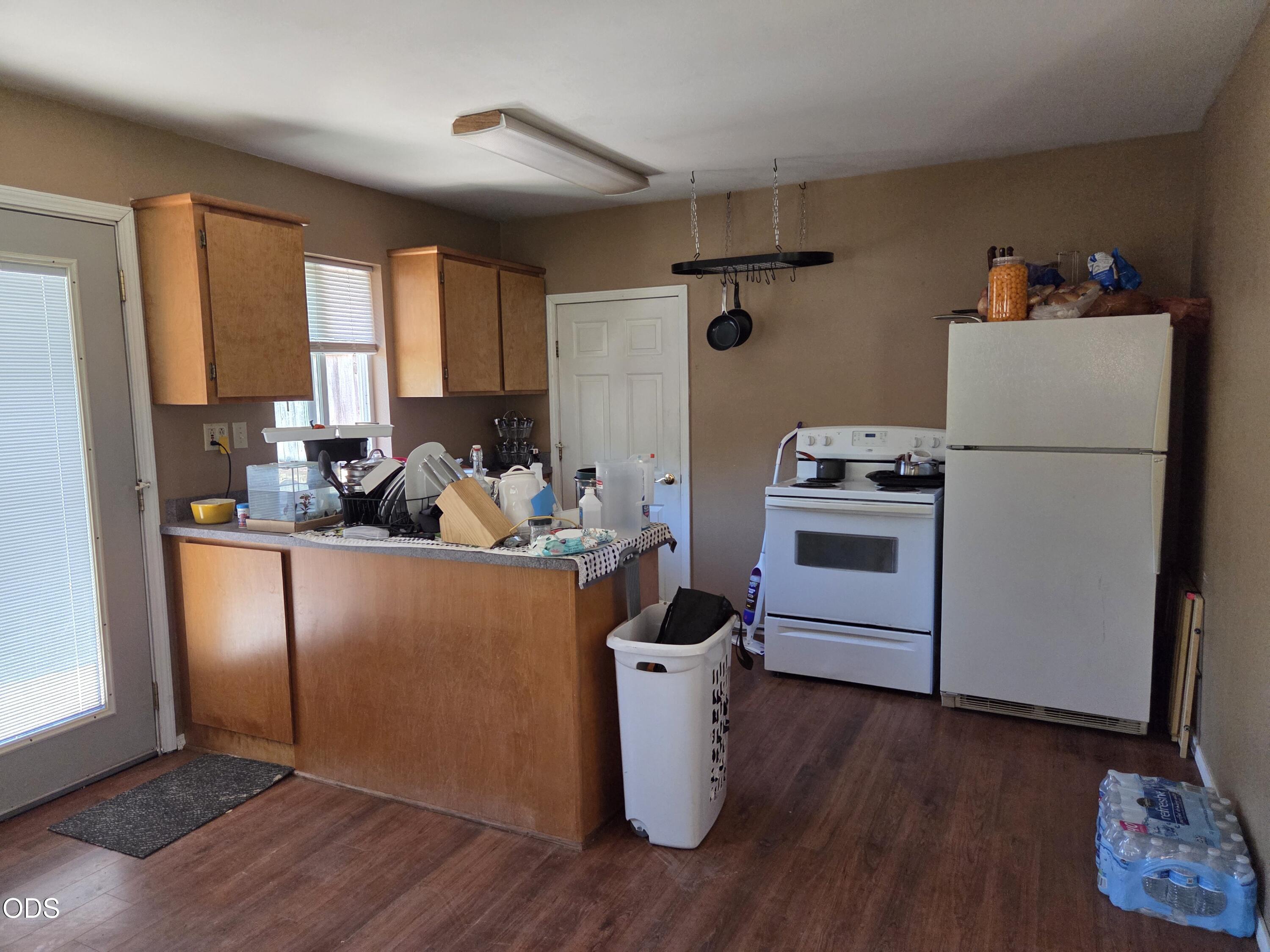 Kitchen with wood cabinets, a crowded peninsula counter, white appliances, and a hanging pot rack.