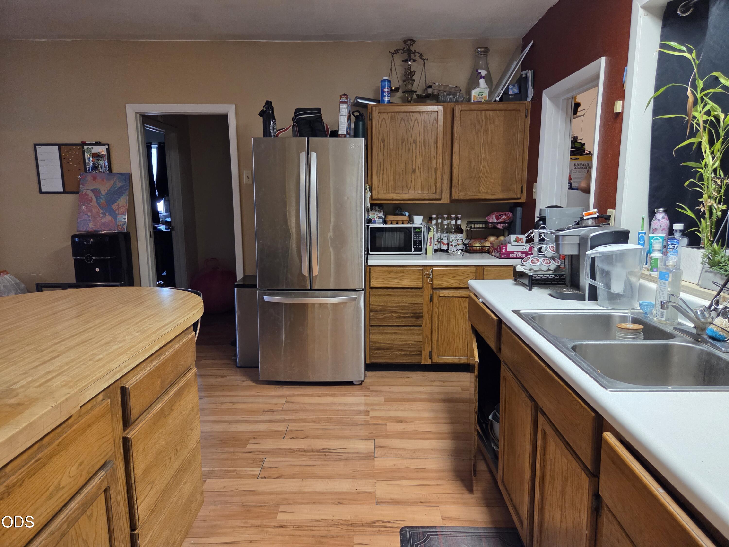 Kitchen with oak cabinets, stainless refrigerator, double sink, and wood-plank flooring.