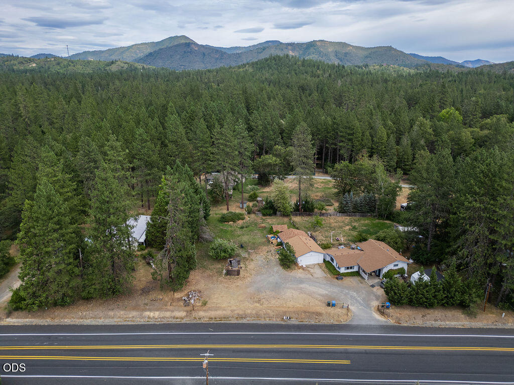 Aerial view of a home beside a road, surrounded by forest with mountains in the distance.