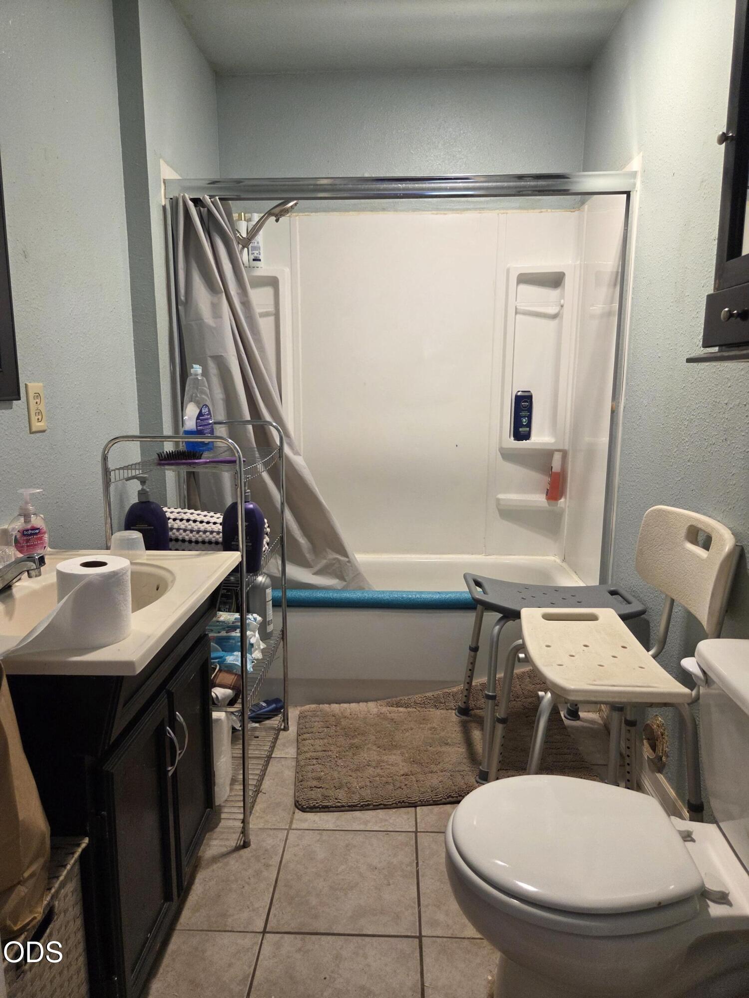 Bathroom with a white shower enclosure, dark vanity, toilet, and two shower chairs.