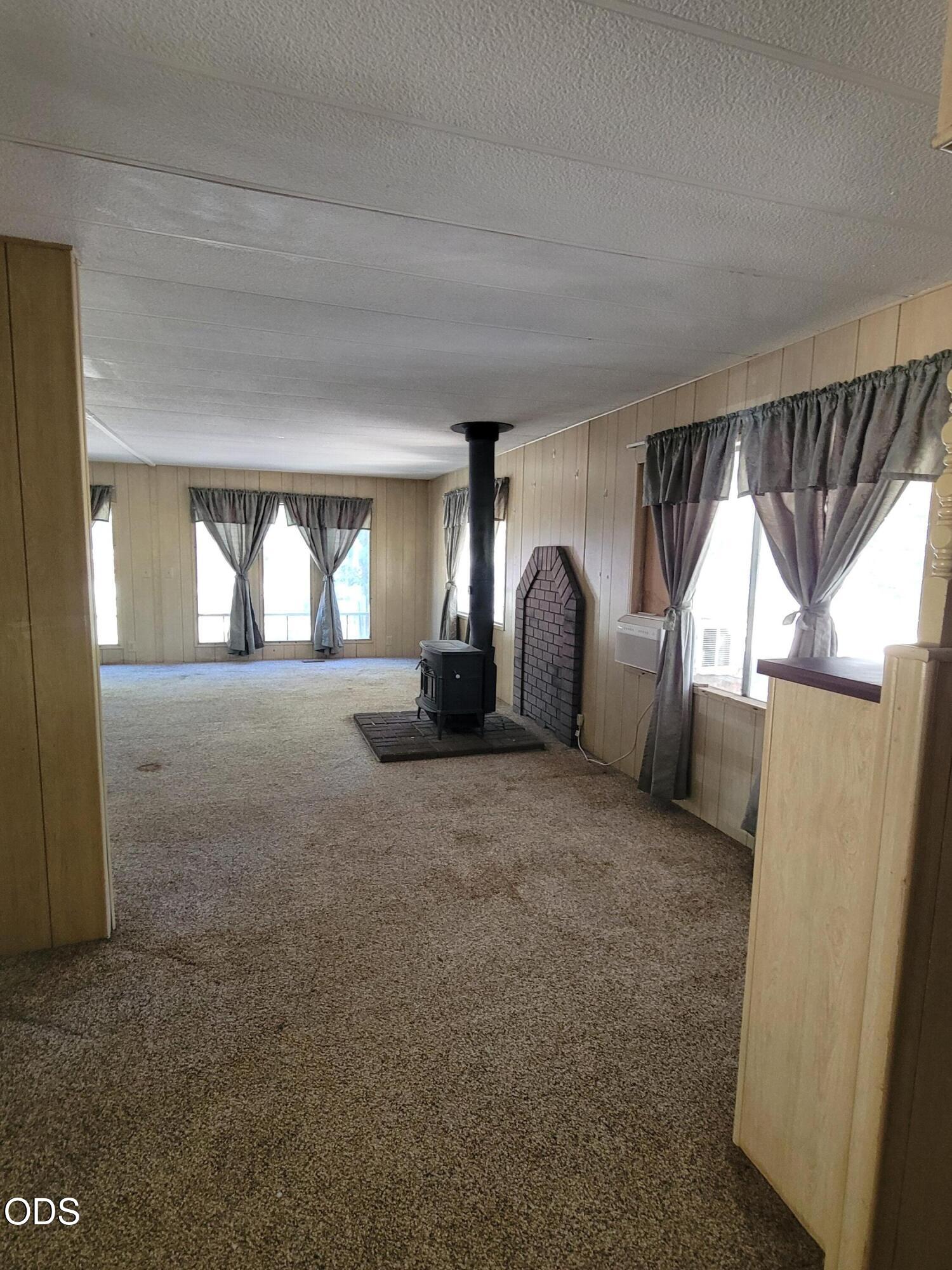 Vacant living room with carpet, curtained windows, and a freestanding wood stove.
