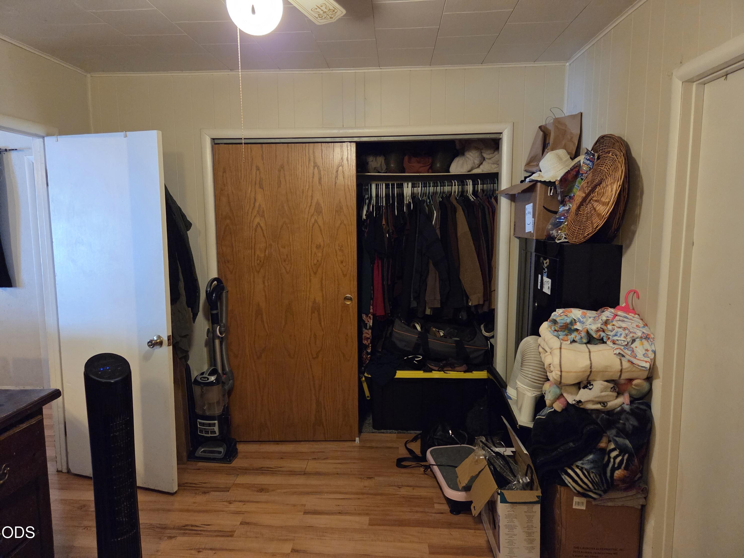Open closet filled with clothes and bags, with a vacuum and stacked blankets nearby.