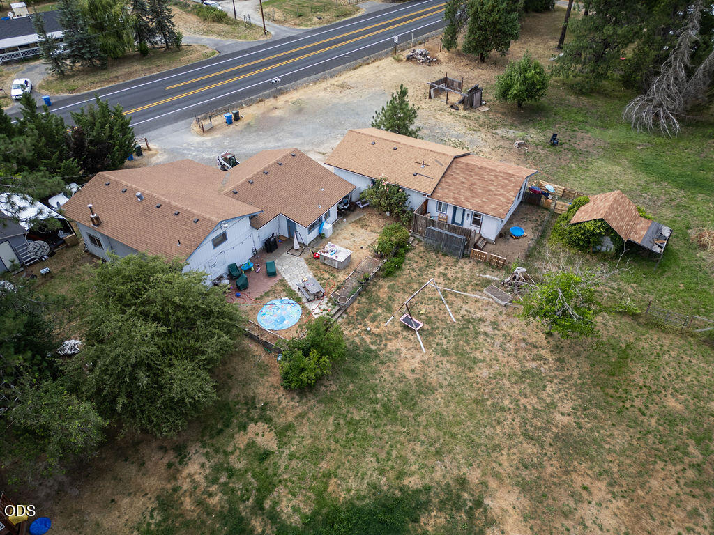 Aerial view of a single-story home, outbuildings, pool, and dry yard beside a road.