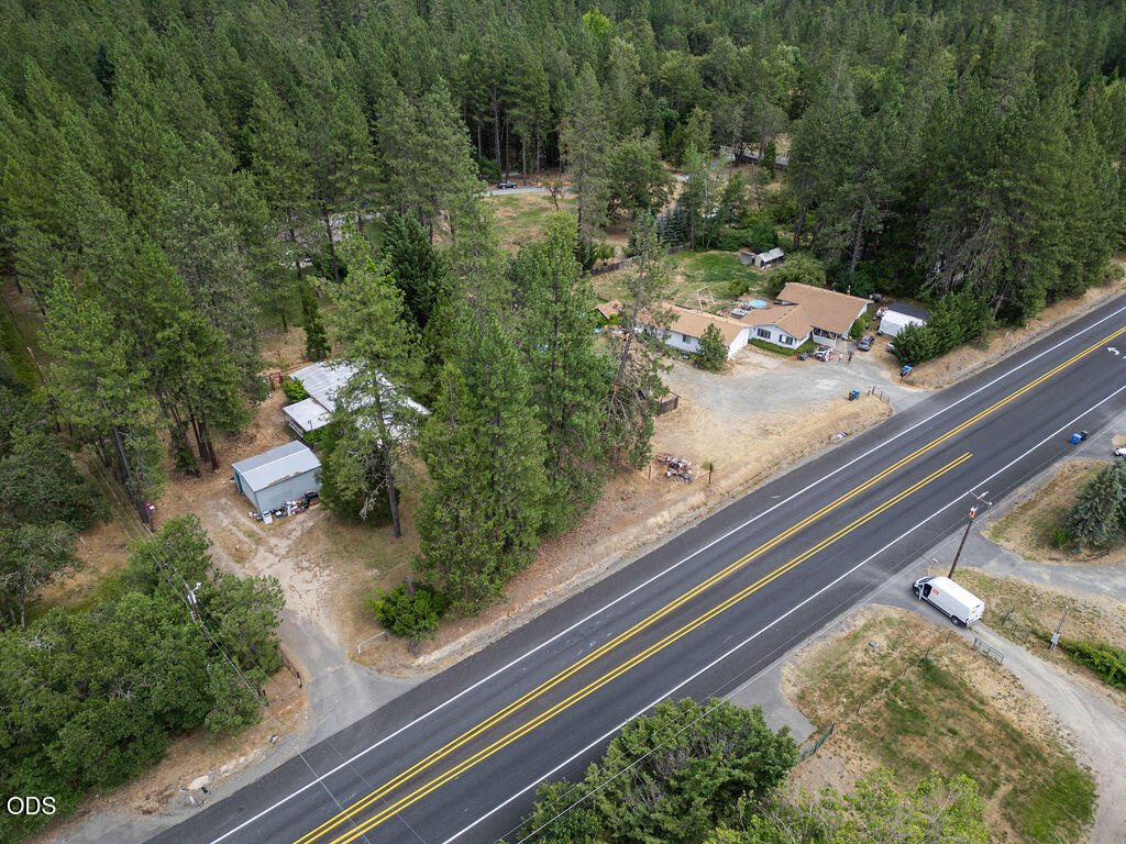 Aerial view of a wooded property with a home, outbuildings, and highway frontage.