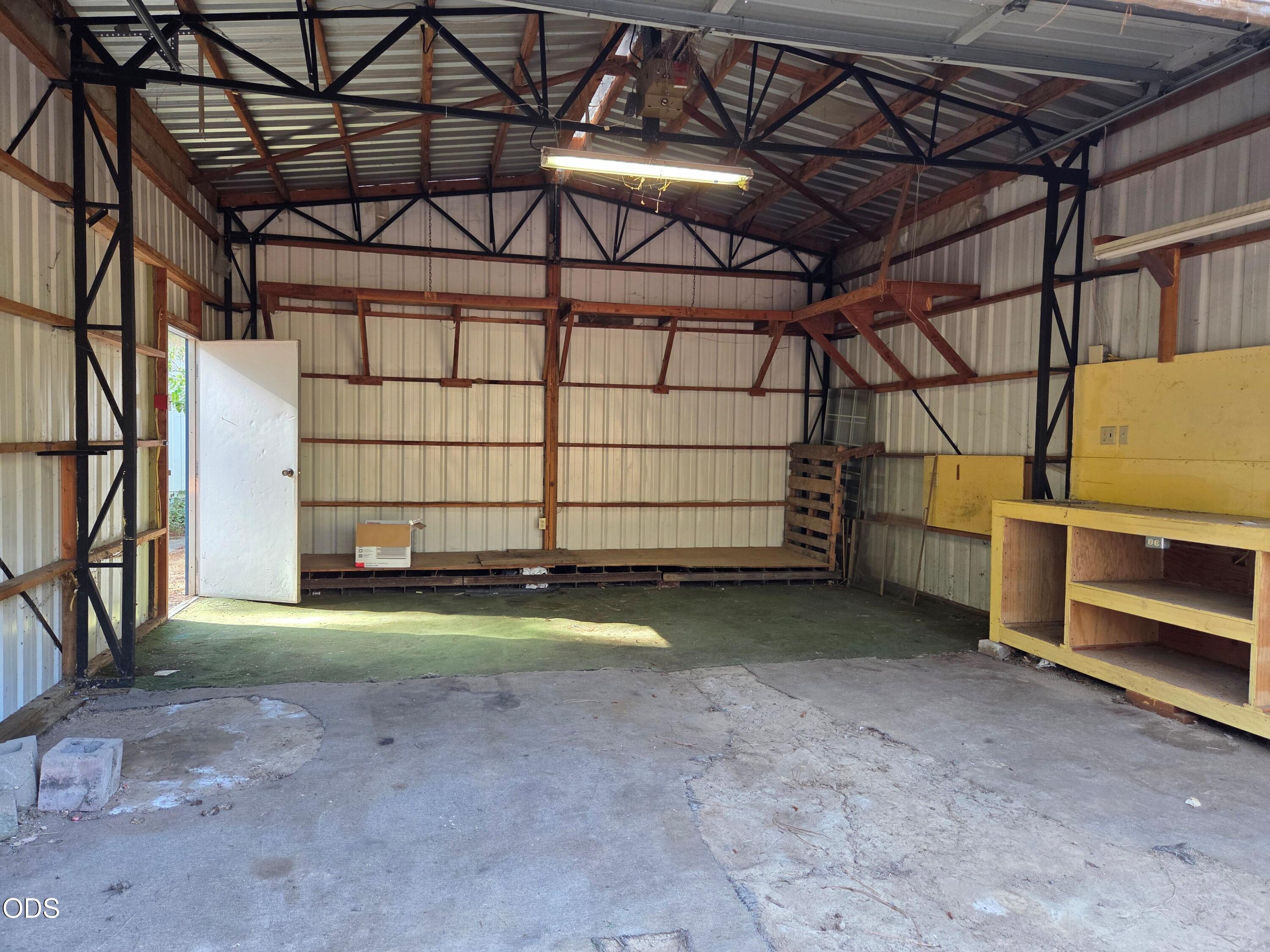 Workshop interior with exposed roof trusses, concrete floor, and yellow workbenches along the wall.