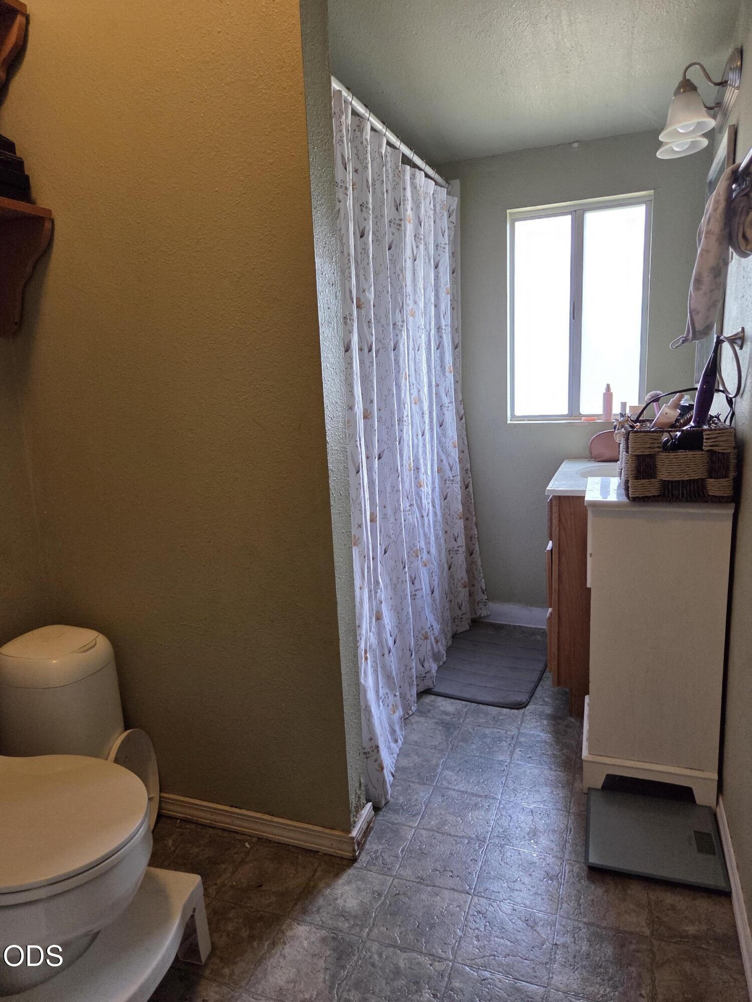 Bathroom with a curtained shower, toilet, and vanity beneath a bright window.