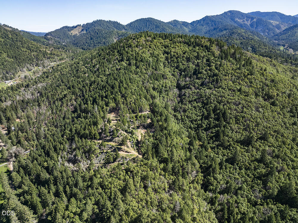 Aerial view of forested mountain property with a small clearing and distant ridgelines.