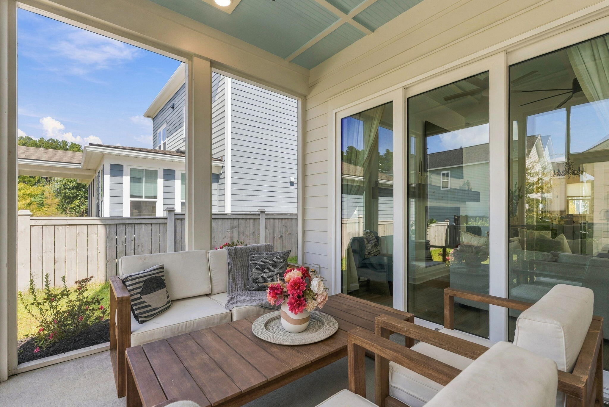 Covered patio with cushioned wood seating, a flower-topped coffee table, and large sliding glass doors.