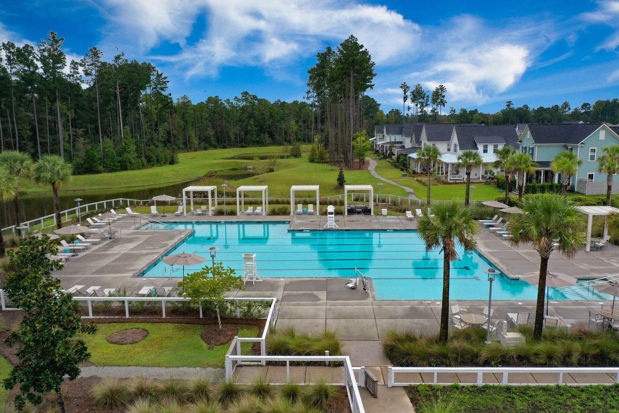 Community swimming pool beside townhomes, with a pond and wooded landscape.