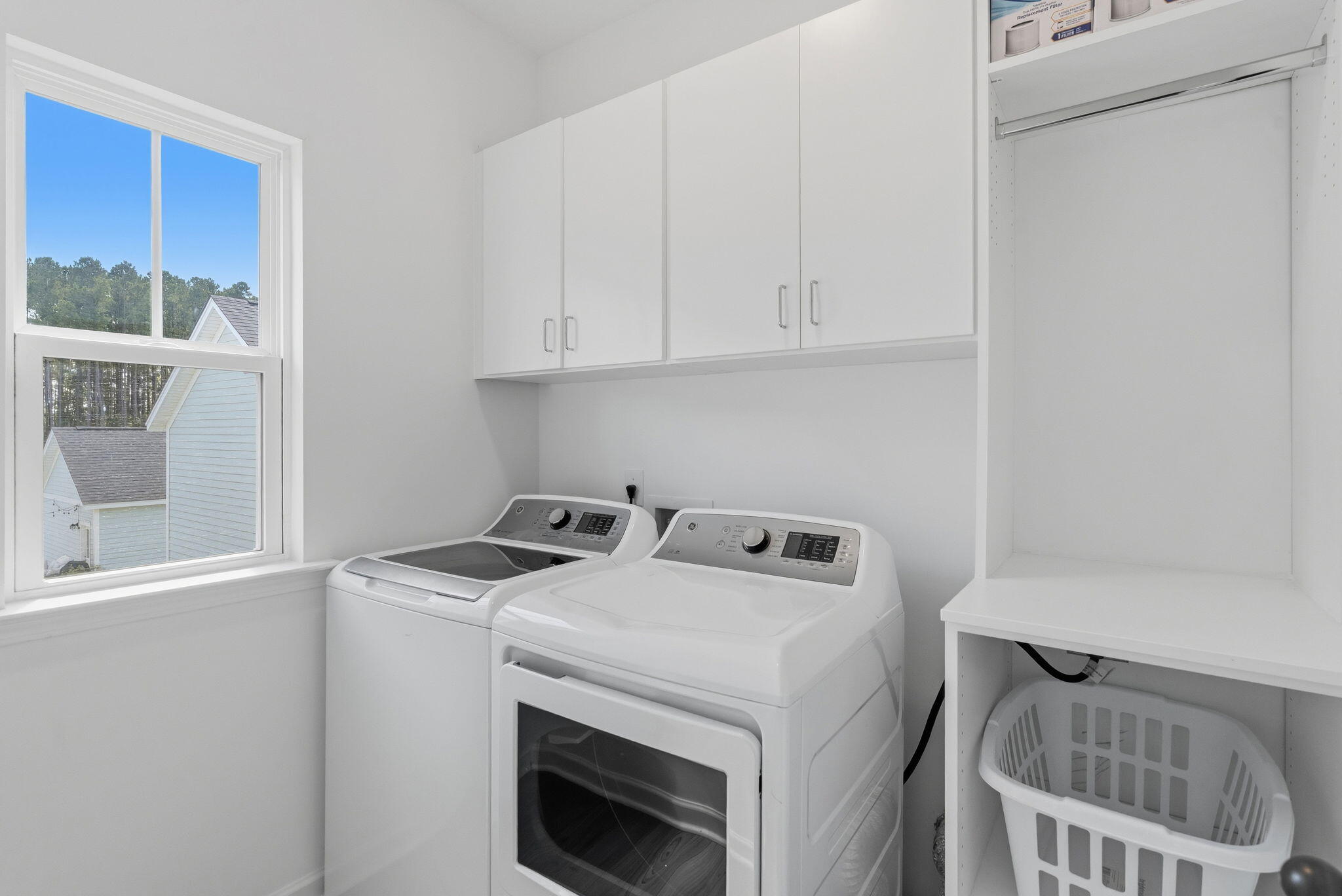 Laundry room with washer and dryer, white cabinets, and a window overlooking neighboring homes.