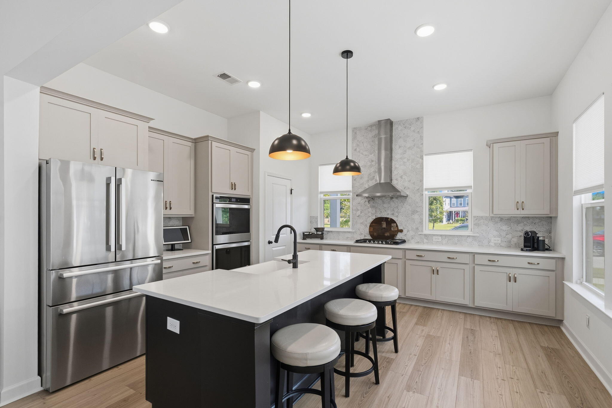 Modern kitchen with a large island, three stools, stainless steel appliances, and patterned backsplash.