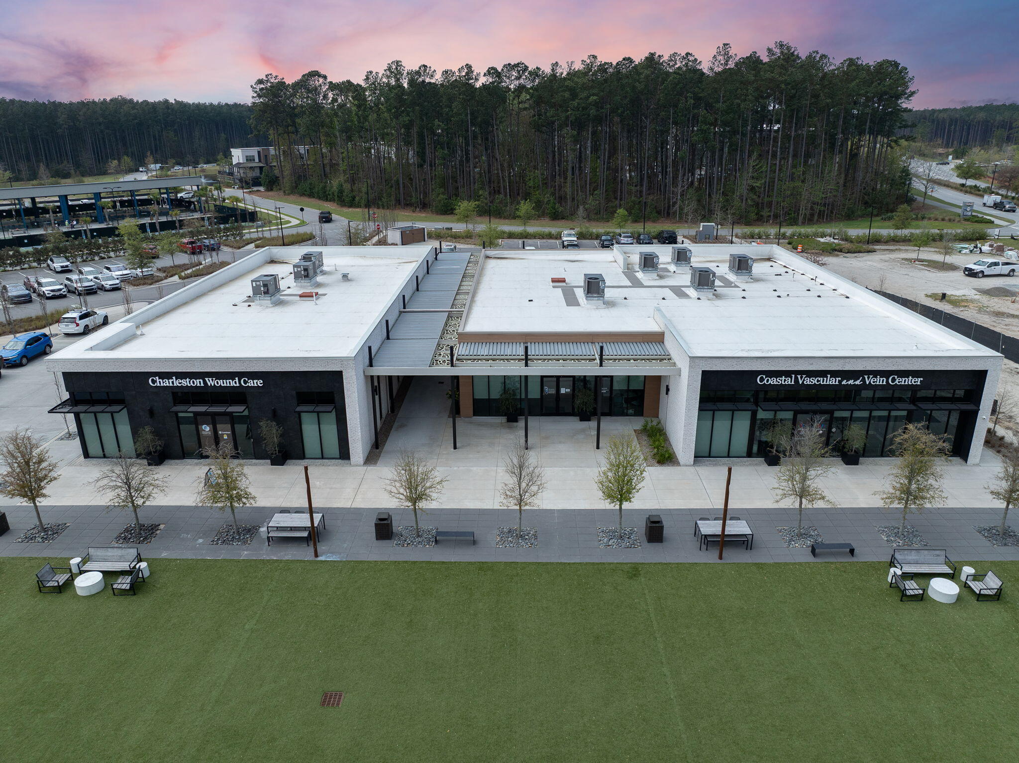 Modern medical office building with two clinic signs, a broad lawn, and outdoor seating.