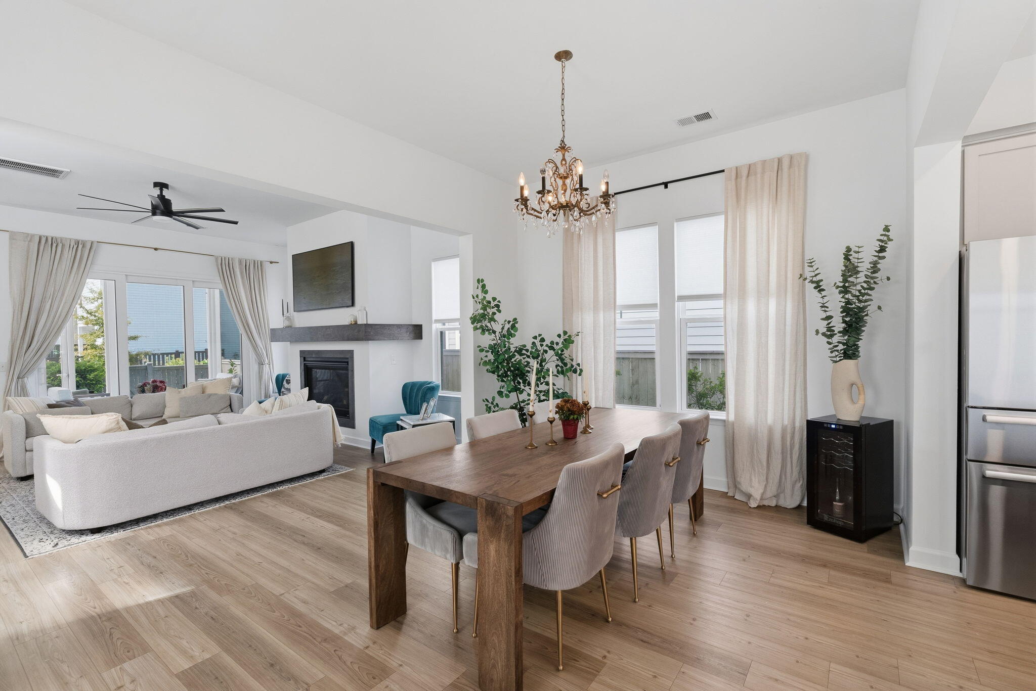 Open-plan living and dining room with a fireplace, wooden table, and tall curtained windows.