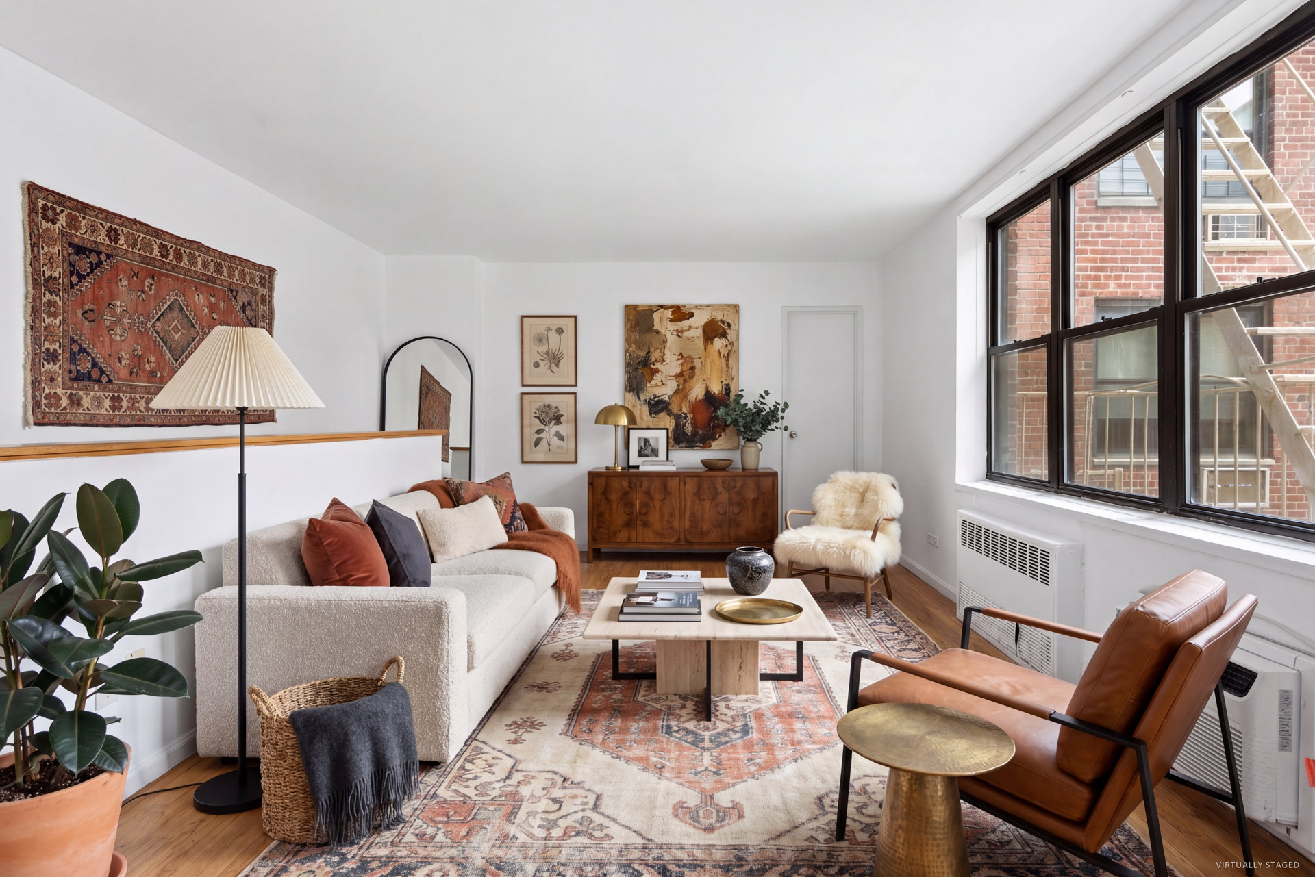 Living room with large windows, a cream sofa, leather chairs, and layered patterned rugs.
