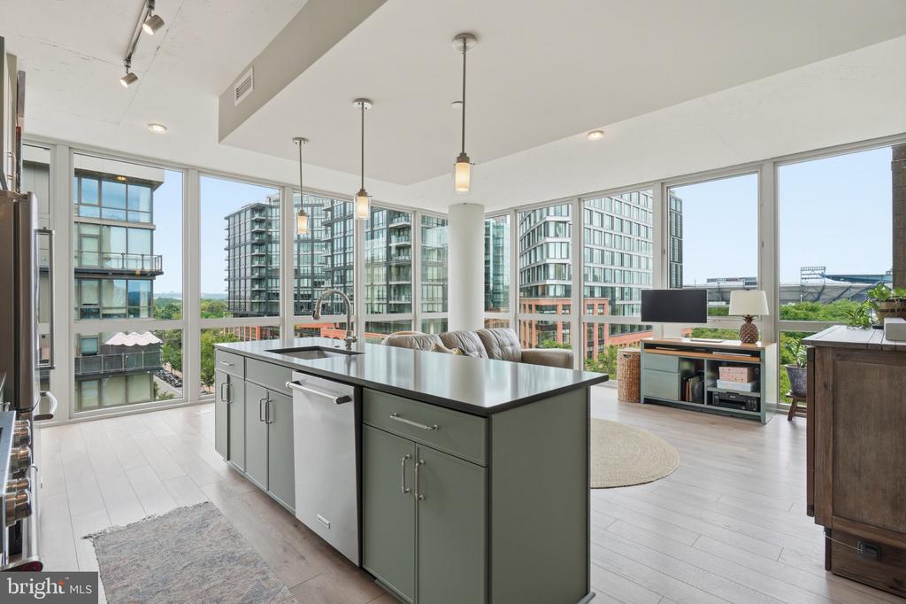 Open-plan condo kitchen with a large gray island and floor-to-ceiling windows overlooking city buildings.