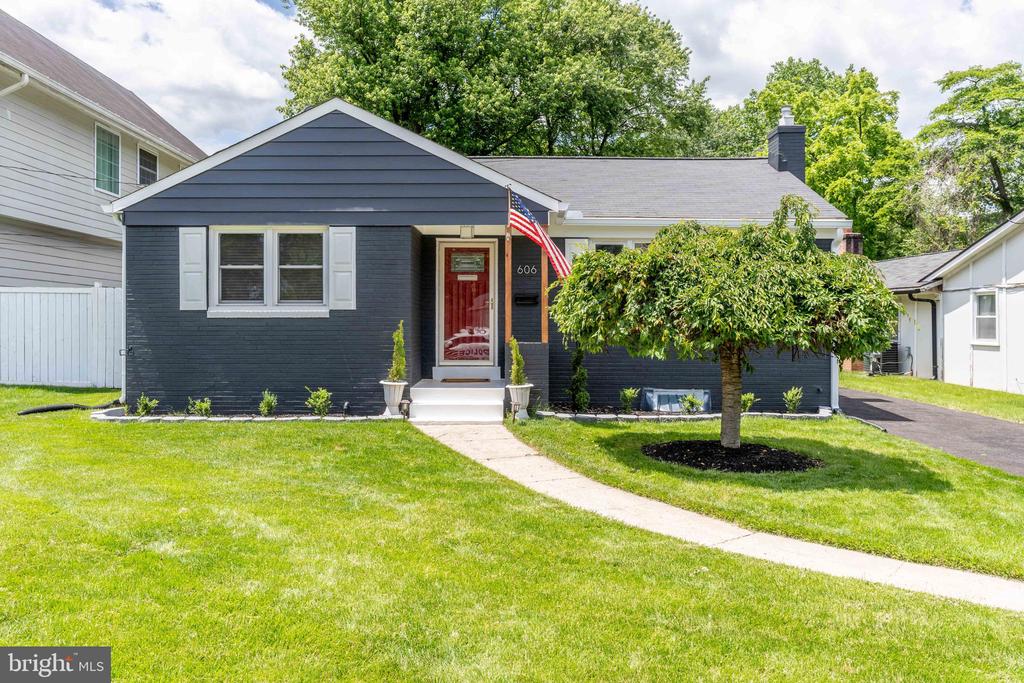 Dark blue bungalow with a red front door, American flag, and a tree-shaded lawn.