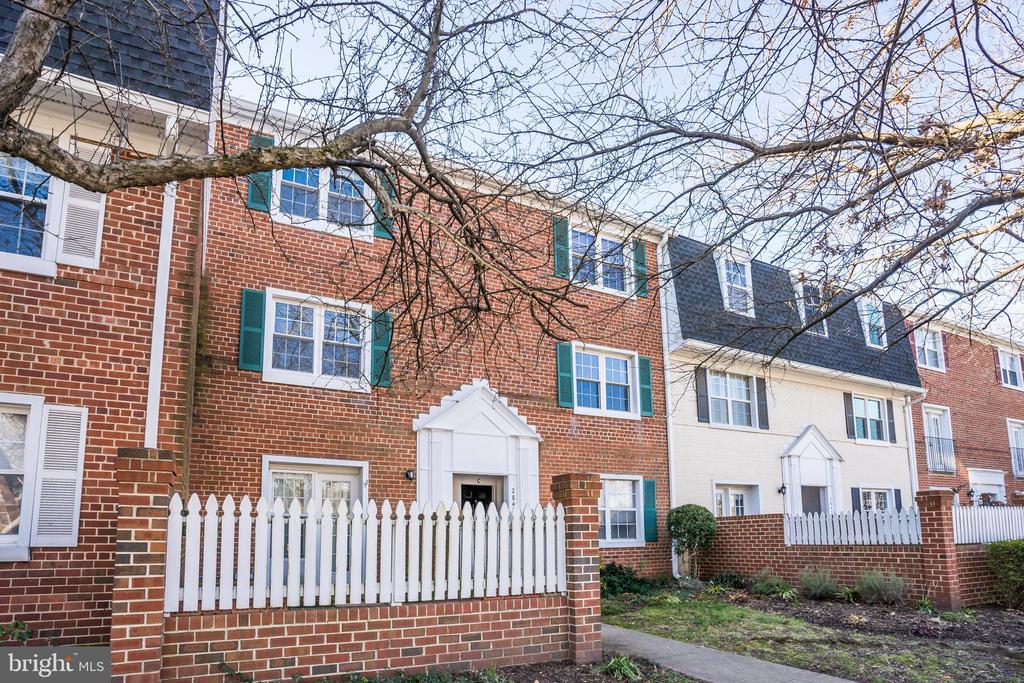 Red-brick rowhouse with green shutters behind a white picket fence and bare tree branches.