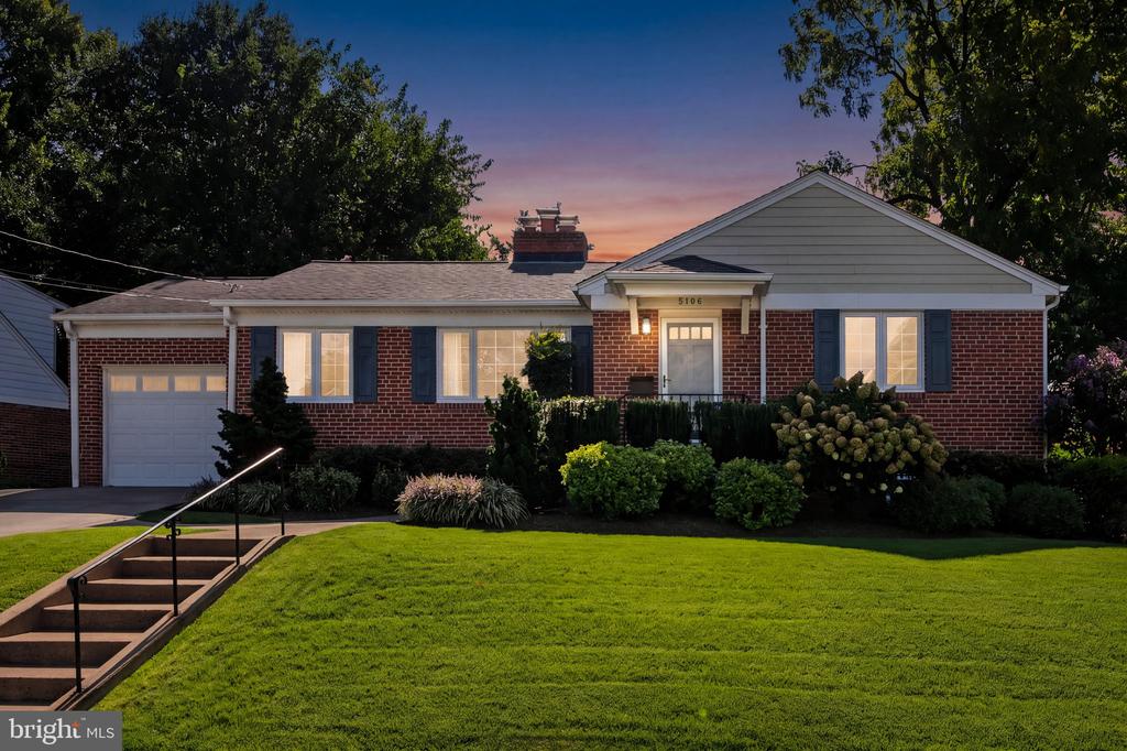 Brick ranch-style home with attached garage and landscaped lawn at dusk.