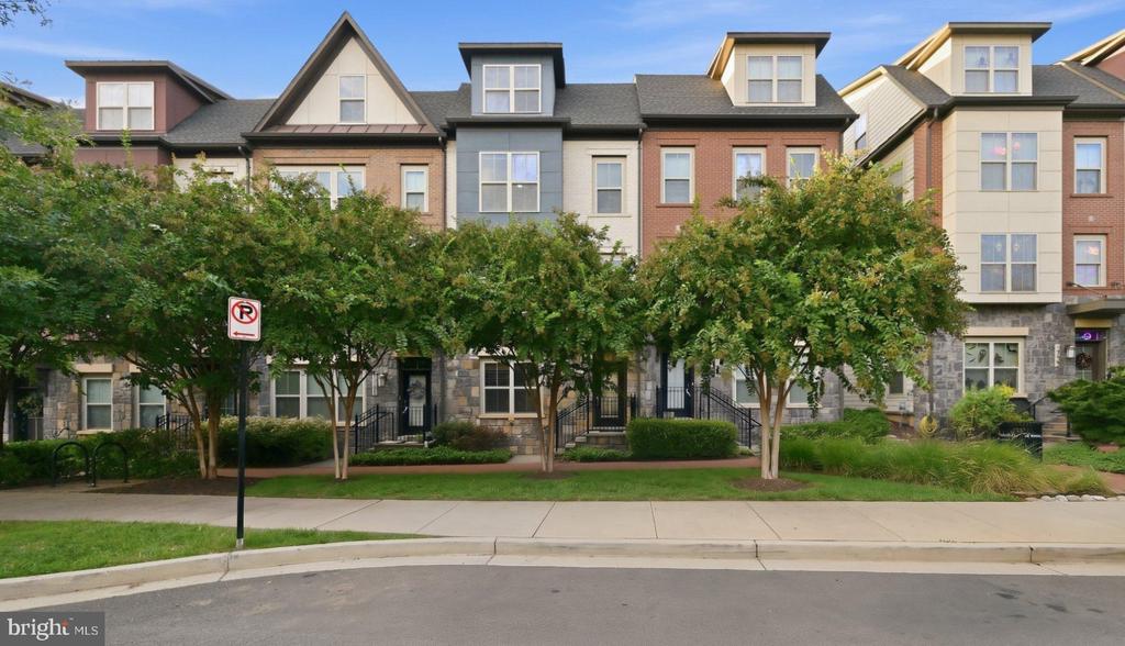 Row of attached townhomes with varied gabled roofs, stone ground floors, and leafy street trees.