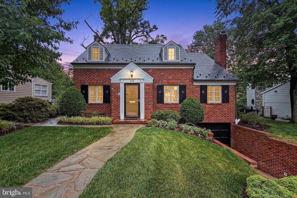 Red-brick house with dormer windows, black shutters, and a stone walkway at dusk.