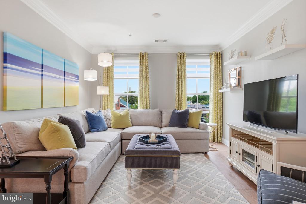 Living room with a pale sectional, colorful cushions, tall windows, and a large abstract painting.