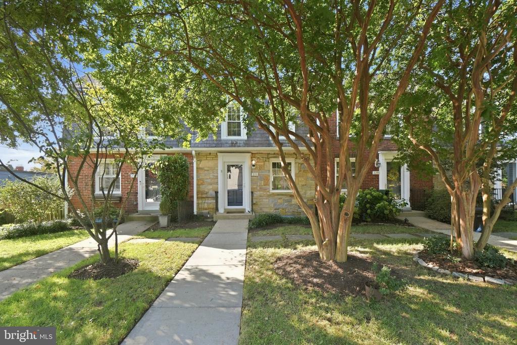 Attached brick and stone home behind mature trees, with a walkway leading to the front door.