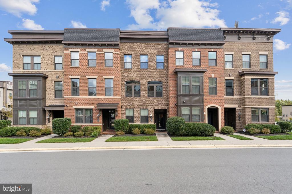 Row of brick townhomes with projecting bay windows and landscaped entryways along a residential street.