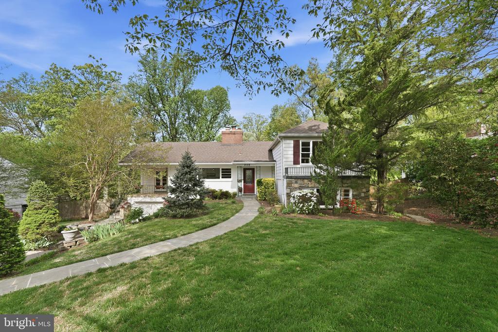 White split-level home with a red front door, brick chimney, and curved walkway through the lawn.