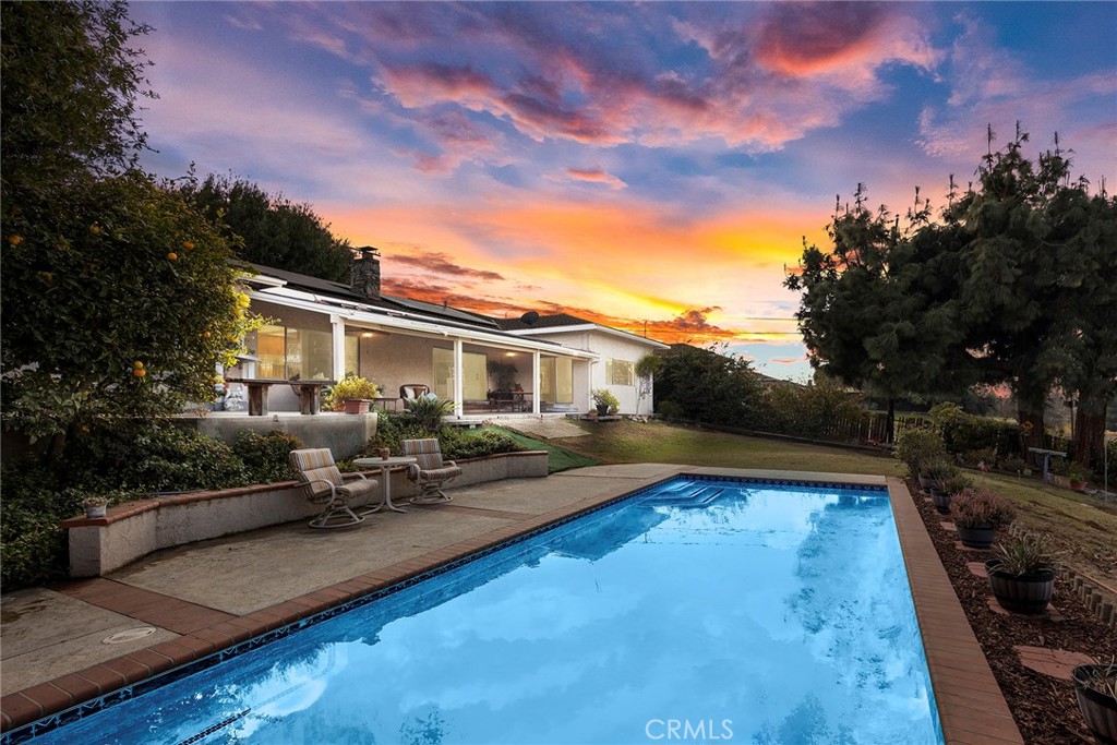 Backyard pool beside a single-story home, with patio seating and a colorful sunset sky.