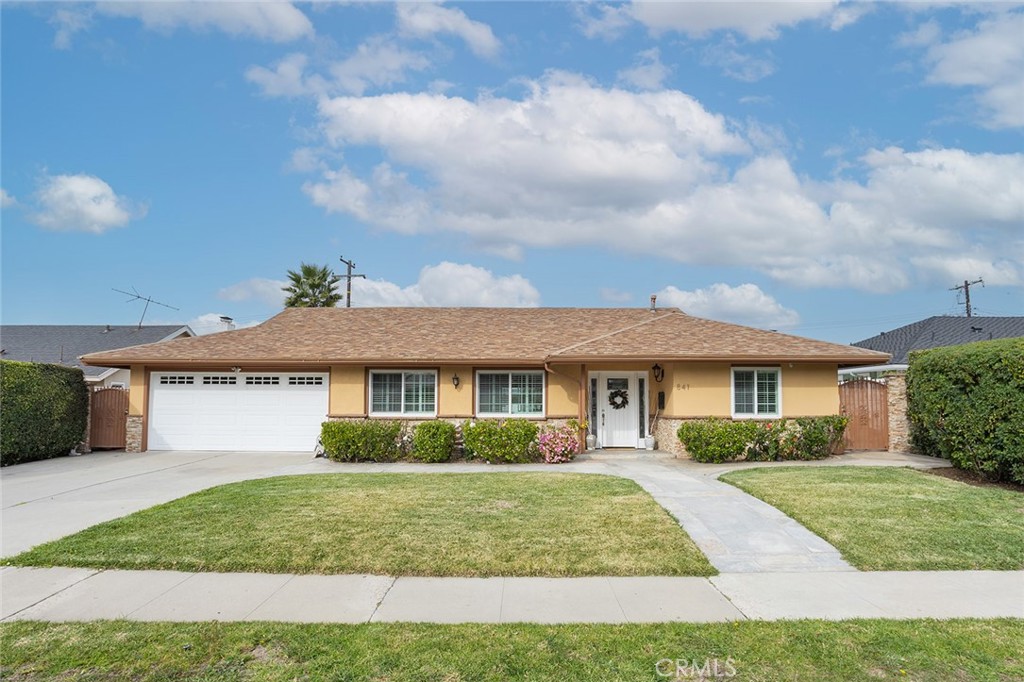 Single-story tan house with a two-car garage, front lawn, and curved walkway.