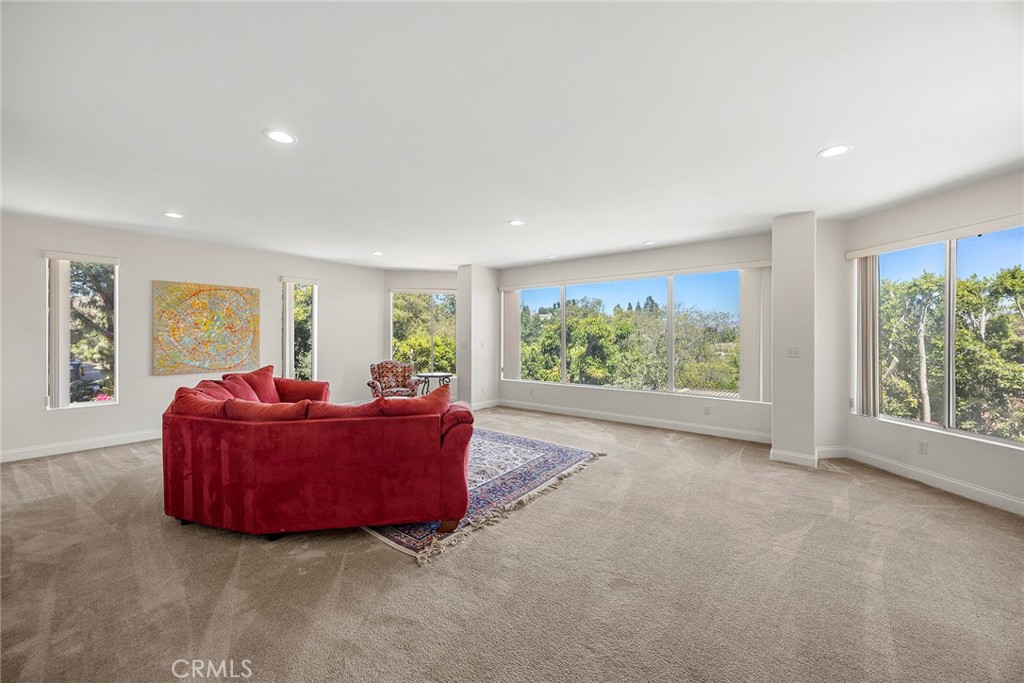 Living room with a red sectional sofa, patterned rug, and large windows overlooking trees.
