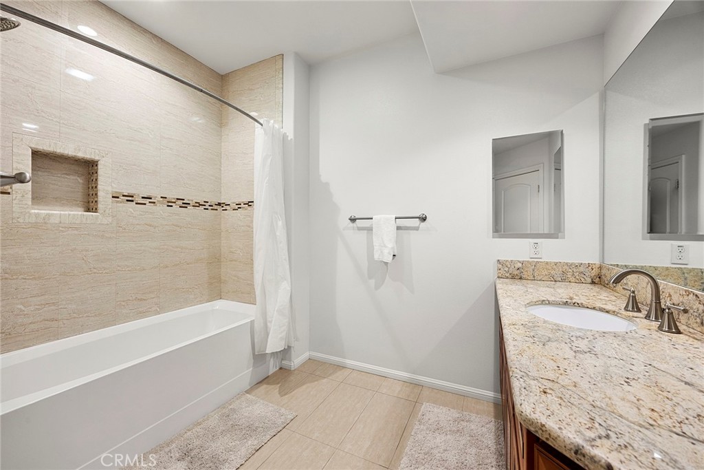 Bathroom with a beige tiled tub and shower and a granite vanity.