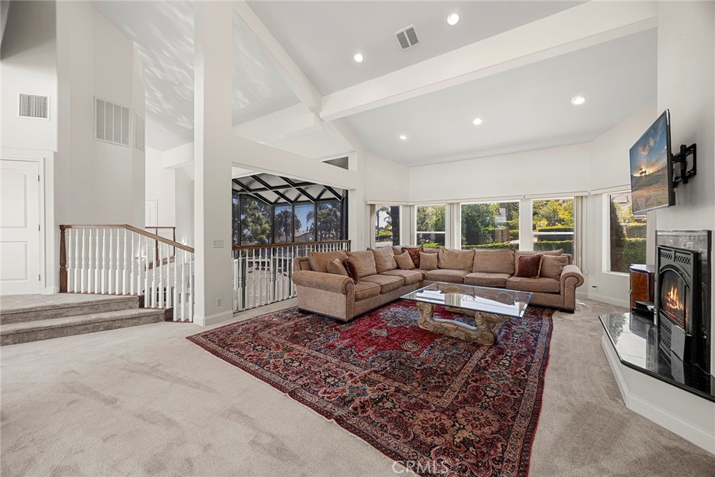Living room with a vaulted ceiling, beige sectional, patterned rug, and fireplace.