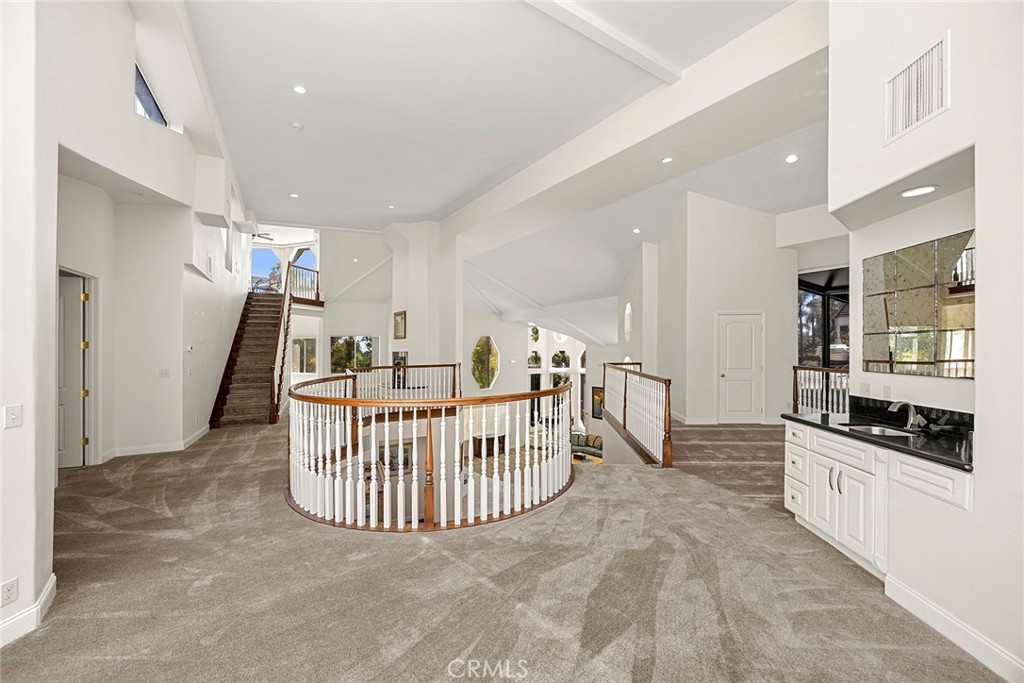 Two-story foyer with vaulted ceiling, curved stairwell railing, carpeted floors, and a built-in sink cabinet.