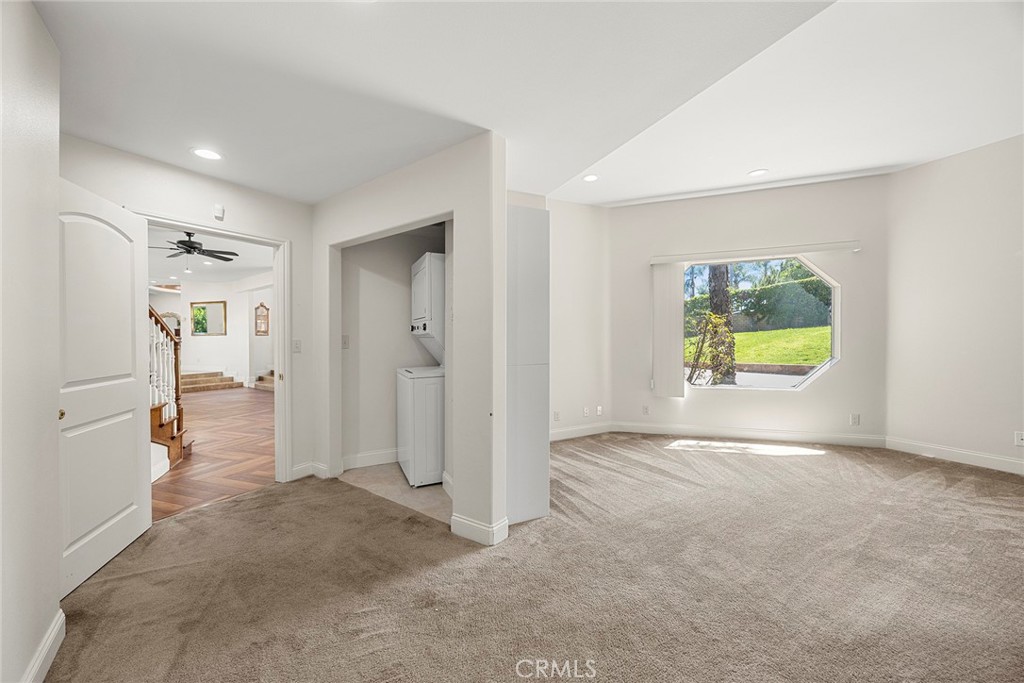 Empty carpeted living room with an octagonal window overlooking a green yard and a laundry alcove.