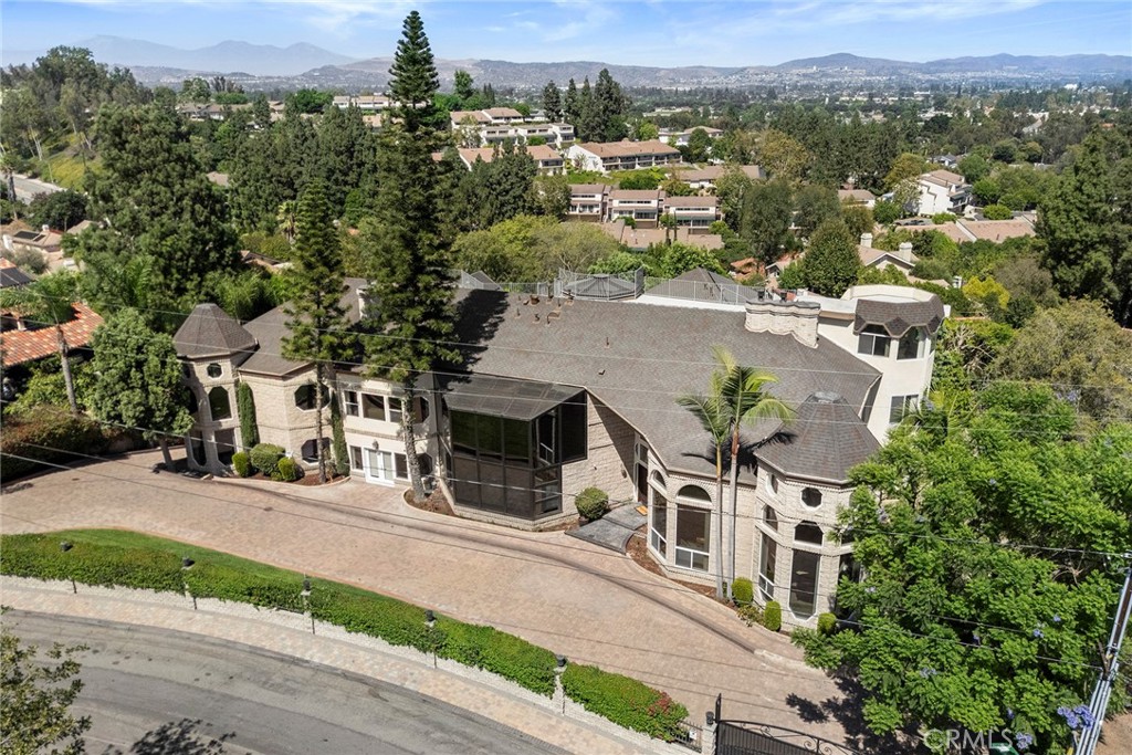 Large stone-and-stucco home with turret-like corners and a gated brick driveway, seen from above.